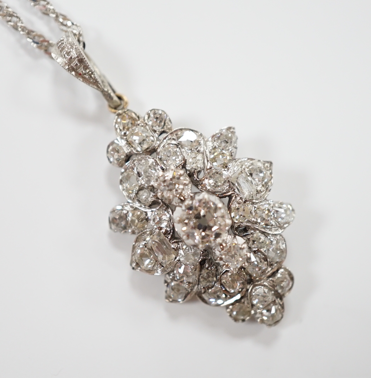 A white metal and diamond cluster set oval pendant, 27mm, on 9kt white metal chain, gross weight 5.8 grams.